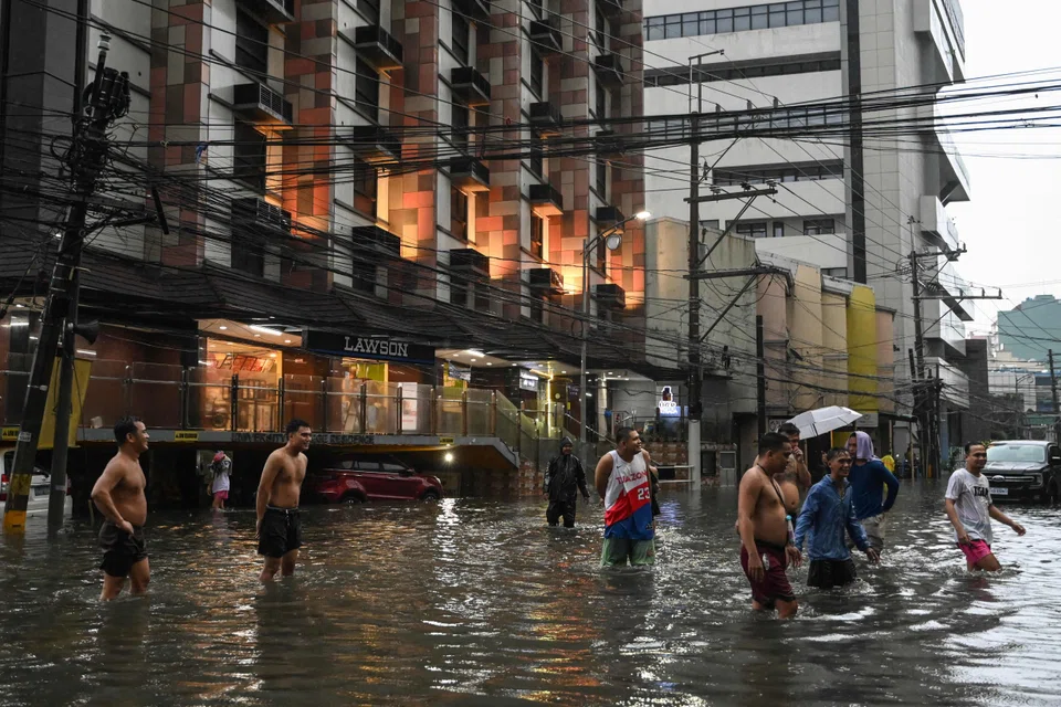 People walk along a flooded street in Manila amid heavy rains brought by Typhoon Gaemi, July 24, 2024.