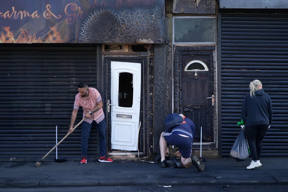 Restaurant owner Luqman Khan clears debris from the street in front of his restaurant in Middlesbrough on Aug 5, following rioting and looting the day before. 