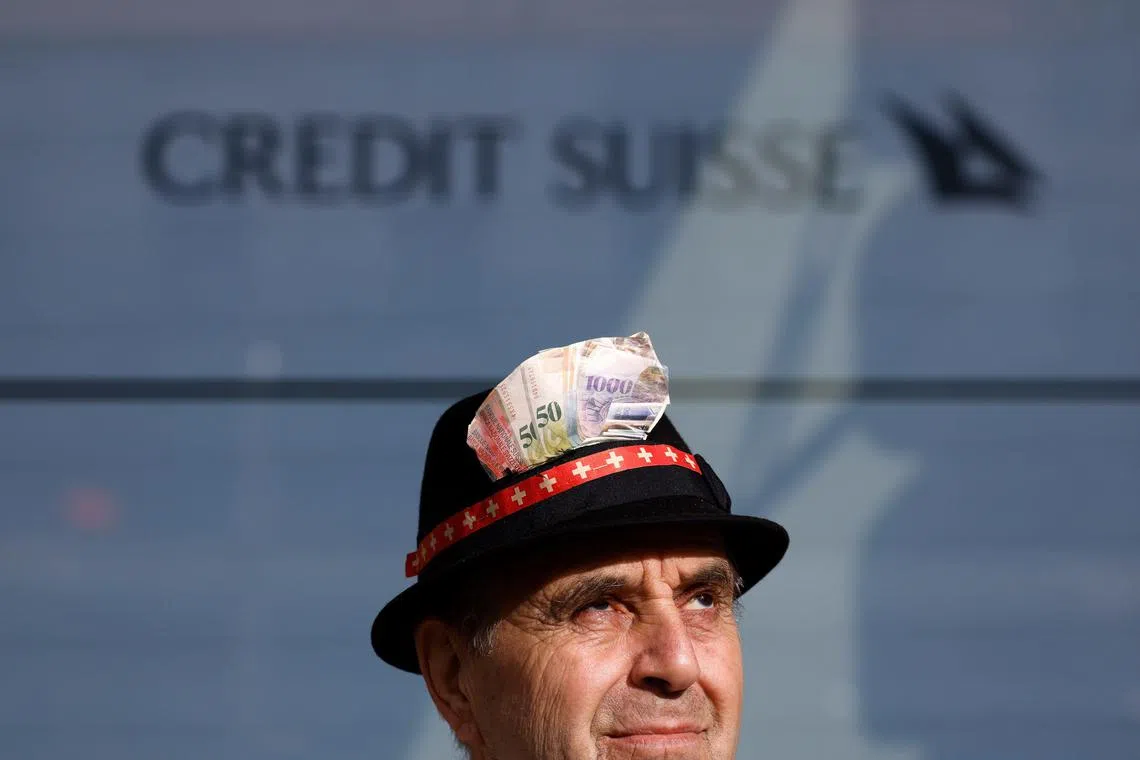 A demonstrator wears a hat adorned with pictures of Swiss franc banknotes outside the Credit Suisse Group headquarters in Zurich, Switzerland, on March 21, 2023. Credit Suisse merchandise went on auction sites as the bank was being taken over by rival UBS.
