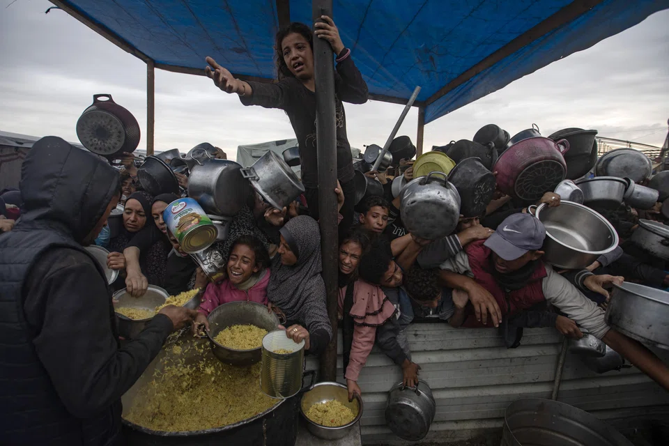 Palestinians, including children, hold metal pots and pans as they gather to receive food cooked by a charity kitchen, in Khan Yunis, southern Gaza Strip, Nov 29, 2024. According to UNRWA, over 1.8 million people across the Gaza Strip are experiencing 'high levels' of acute food insecurity, including around 133,000 people facing 'catastrophic' food insecurity, with acute malnutrition ten times higher than before the war. 