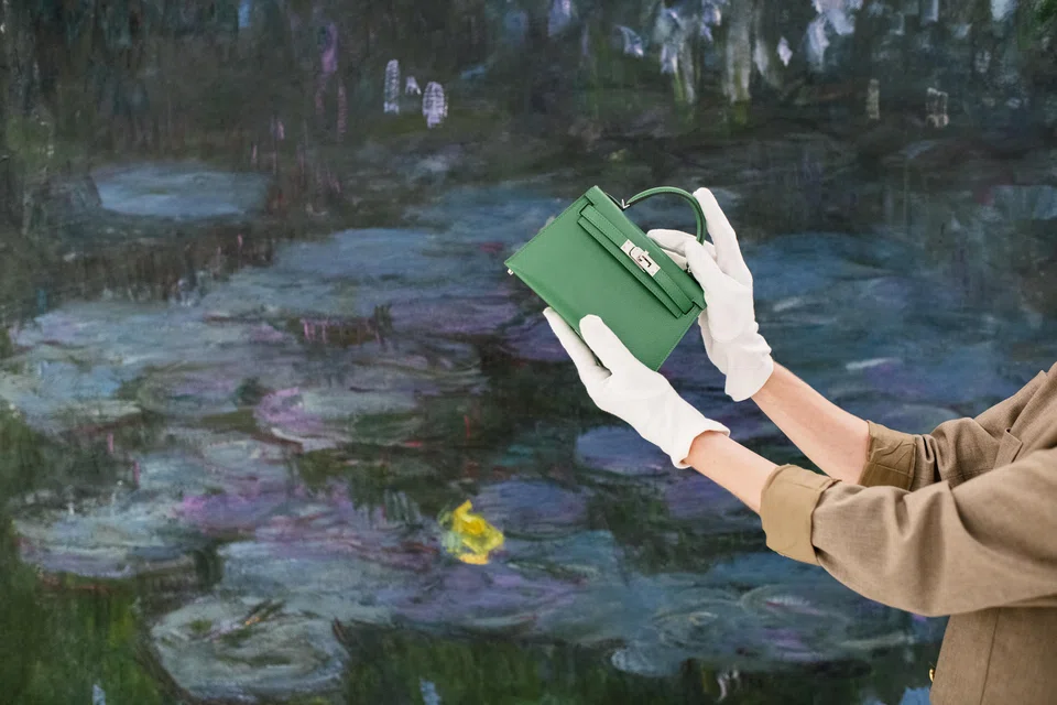 Aurelie Vassy, Sotheby’s head of handbag and fashion sales in Europe, holds a Hermes mini Kelly Bags in front of a Claude Monet painting, at the auction house’s new Paris headquarters on Oct 12, 2024.