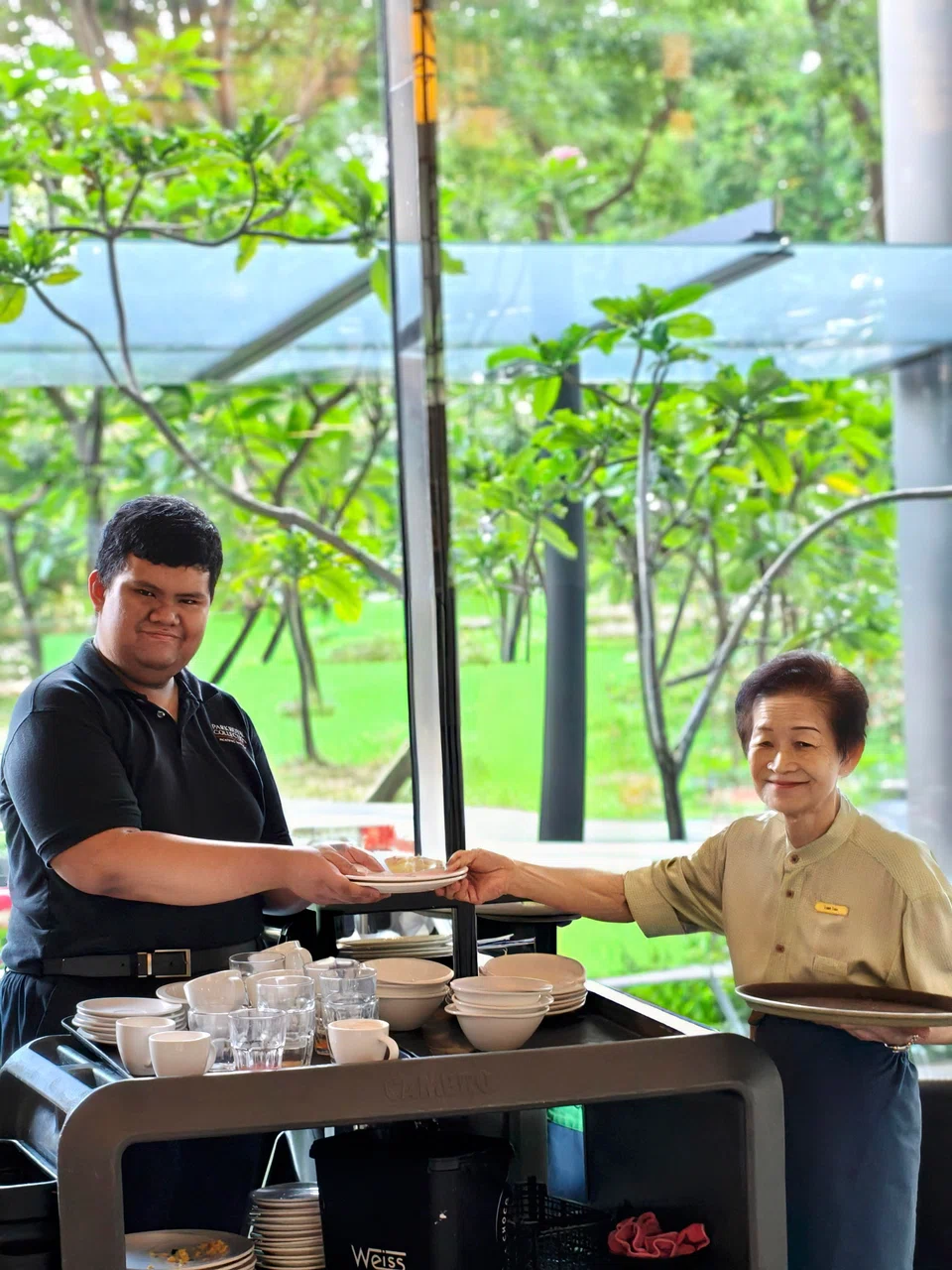 Dave Burgos Abelinde (left), a PWD working in F&B services, often helps mature worker Tan Lian Tee carry heavy things when they work together at ParkRoyal Collection Pickering’s buffet restaurant.