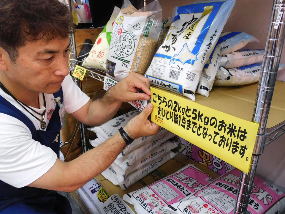 A supermarket worker in Tokyo putting up a sign informing customers purchasing rice to buy only one bag per person. 