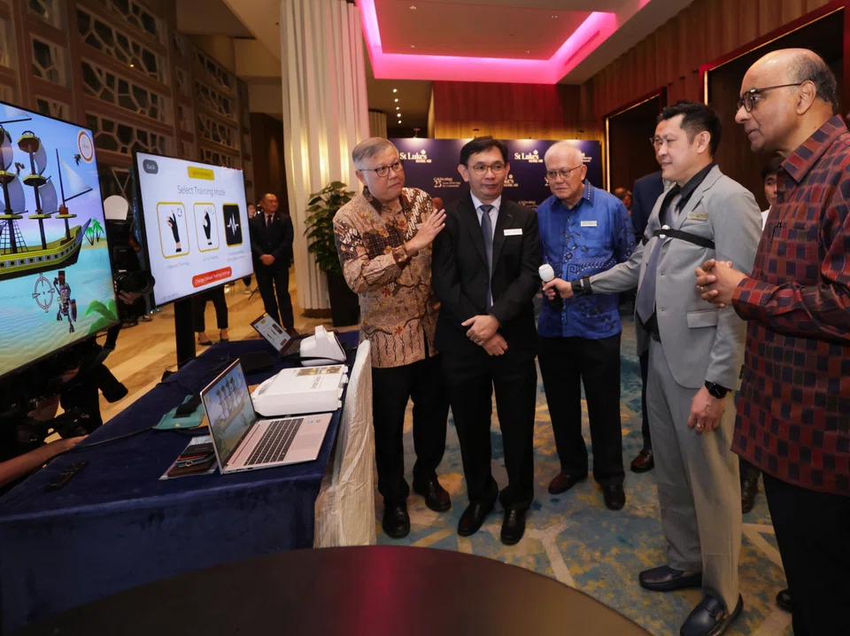 President Tharman Shanmugaratnam watching a demonstration by Jonathan Coo (second from right), a senior occupational therapist, at the robotics rehab therapy booth during SLEC's 25th anniversary gala dinner. With them are (from left) Professor Ho Yew Kee, SLEC chairman; Dave Leong, senior occupational therapist; and Foong Daw Ching (in blue top), SLEC vice-chairman.