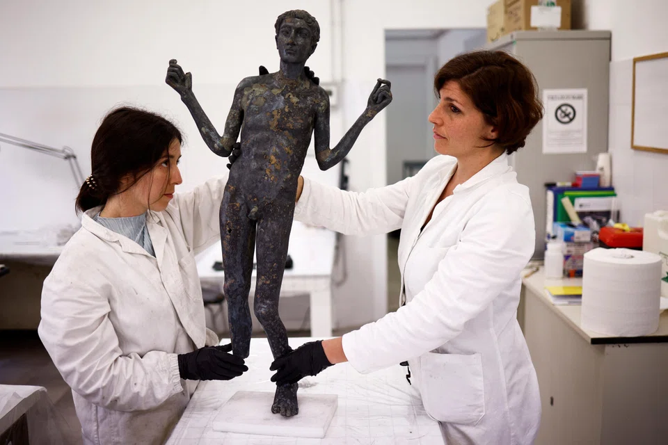 Restorers hold the full-body sculpture of a young Roman apparently suffering from bone disease, after it was discovered and pulled out from the muddy ruins of an ancient spa in San Casciano dei Bagni.