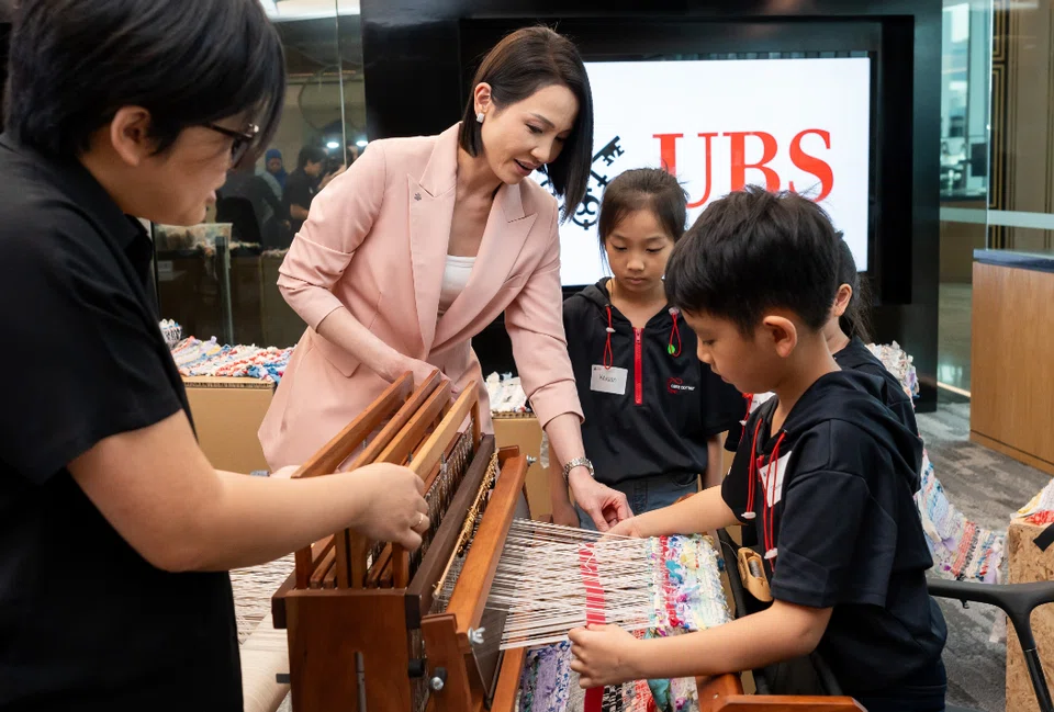 Young Jin Yee (in pink), co-head of UBS global wealth management Asia-Pacific and country head at UBS Singapore, with Care Corner students as they weave a 60-metre-long tapestry as part of the Art for All programme.