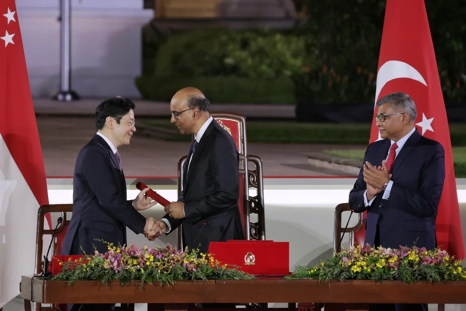 Prime Minister Lawrence Wong receiving the instrument of appointment from President Tharman Shanmugaratnam during the swearing-in ceremony at the Istana on May 15. With them is Chief Justice Sundaresh Menon. 