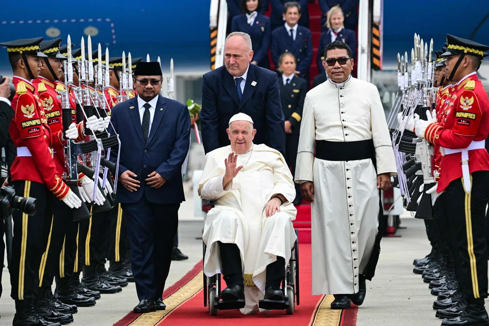 Pope Francis (centre, in wheelchair) is welcomed during his arrival at Soekarno–Hatta International Airport in Jakarta on Sep 3, 2024. .