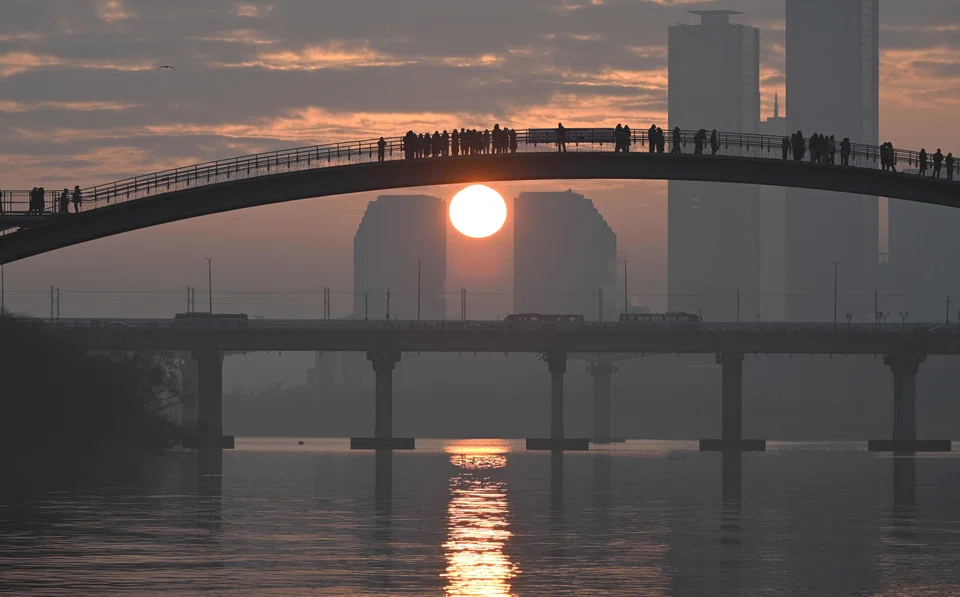 People watch the first sunrise of the new year from a footbridge overlooking the city skyline in Seoul on January 1, 2024. (Photo by Jung Yeon-je / AFP)