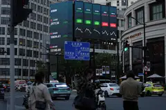 A giant screen displays stock indexes in Shanghai. At least 80 companies listed in mainland China are in danger of triggering delisting thresholds linked to finances, according to Caixin calculations.