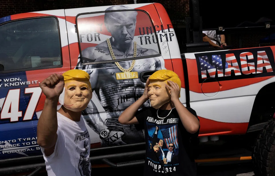 Supporters of Republican presidential nominee and former President Donald Trump pose with his masks as they wait in line to attend a campaign rally during a hot and humid day in Harrisburg, Pennsylvania., July 31, 2024.
