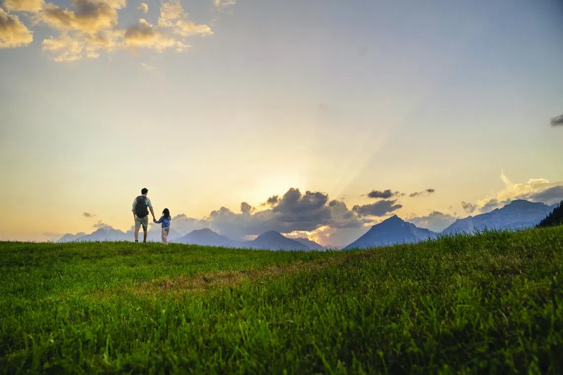 Father and daughter exploring in meadow by mountain range