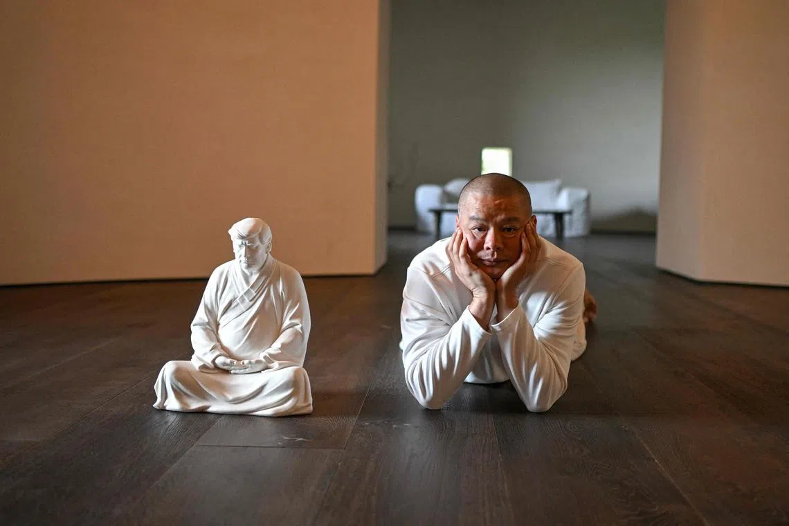 Artist Hong Jinshi posing for photos next to a sculpture of US president-elect Donald Trump in a pose evoking the Buddha at his workshop in Xiamen, in southeastern China's Fujian province. 