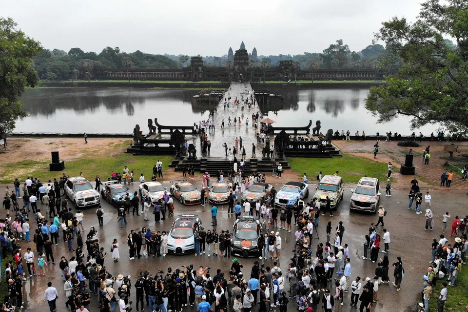 People look at supercars taking part in the Gumball 3000 rally, a motoring event founded by British entrepreneur Maximillion Cooper where participants drive their vehicles some 4,828 kms across multiple countries, parked in front of the Angkor Wat temple.