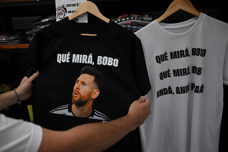 A man holds a t-shirt with an image of Argentine forward Lionel Messi and a phrase reading "What are you looking at, you fool?" at a store in Buenos Aires, Dec 12, 2022. 
