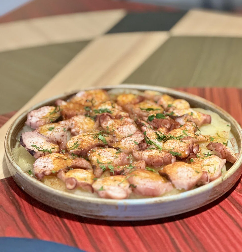 Sliced octopus and potato are served on a hot plate.