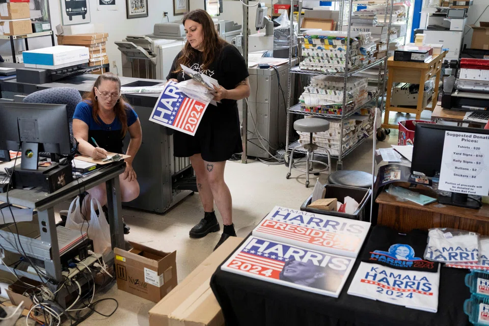 Printshop assistant Melanie Fisher speaks with graphic artist Rainbow Southard about requests for different sizes of campaign buttons in support of US Vice-President Kamala Harris' presidential campaign at the Gloo Factory in Tucson, Arizona, July 25, 2024. 