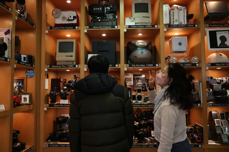 Visitors viewing items inside Extinct Media Museum. It  showcases a collection of gadgets including old cameras, cassette tapes and cell phones.
