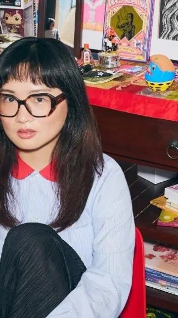 Viral TikTok anthropologist Ashley Chin, known for her deep dives into Singapore ghost stories, sits in an eclectic home setting.