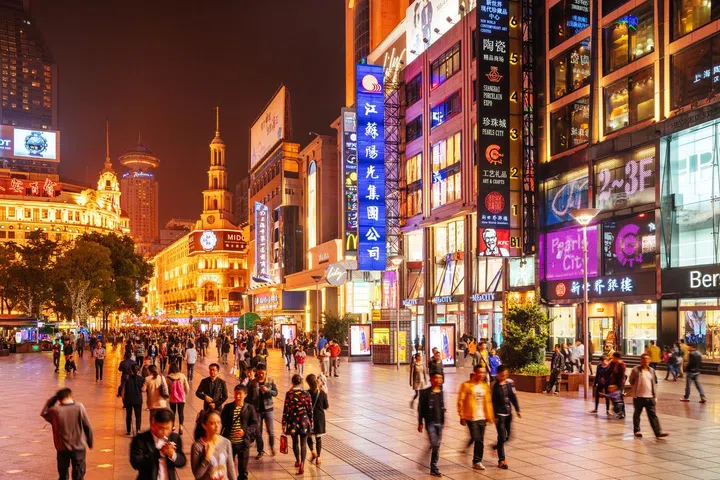 Crowds walk below neon signs on Nanjing Road. The street is the main shopping district of the city and one of the world's busiest shopping districts.