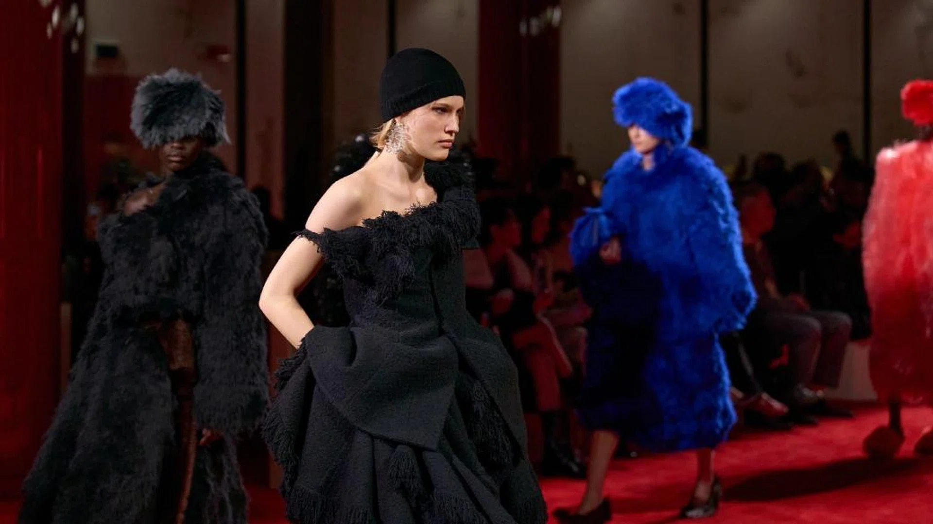  Models walking the runway for the Bottega Veneta Winter Fall 2026 finale, showcasing avant garde textured coats in vibrant blue, red, and black with sculptural silhouettes and fringed detailing.
