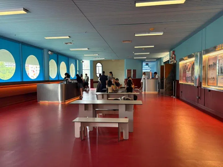 Interior shot of the modern Filmhouse Singapore lobby featuring a retro-futuristic design with red floors, light blue walls, porthole-style windows, and minimalist seating.