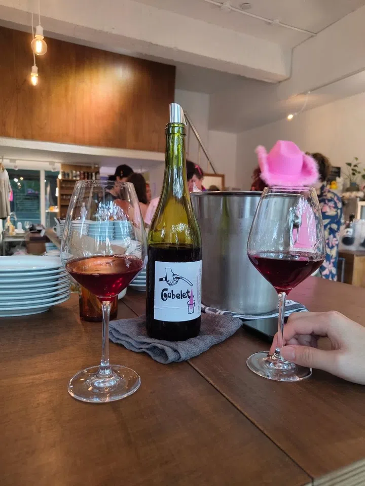 Natural wine bottle from Gobelet served with two glasses at 小泉自然酒 & Saison bar, a trendy minimalist wine bar in Taipei with warm wood interiors and industrial lighting.