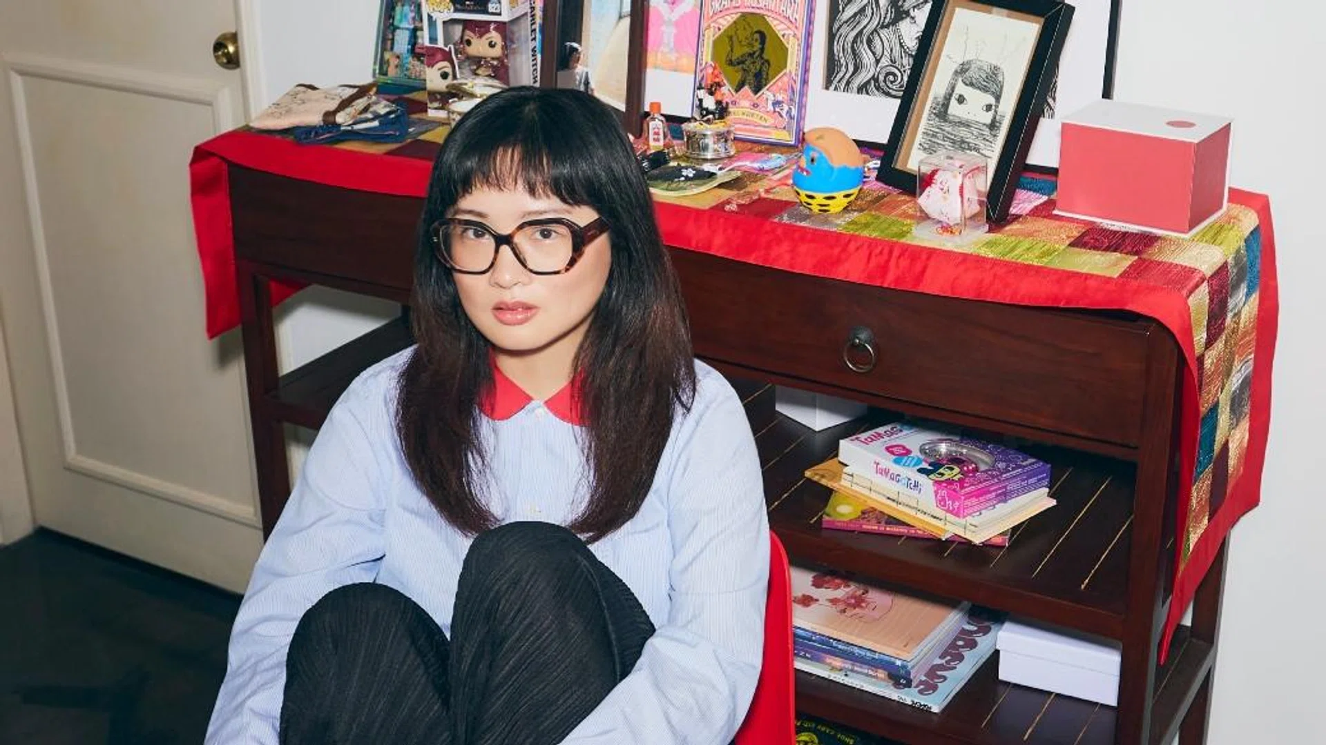 Viral TikTok anthropologist Ashley Chin, known for her deep dives into Singapore ghost stories, sits in an eclectic home setting.