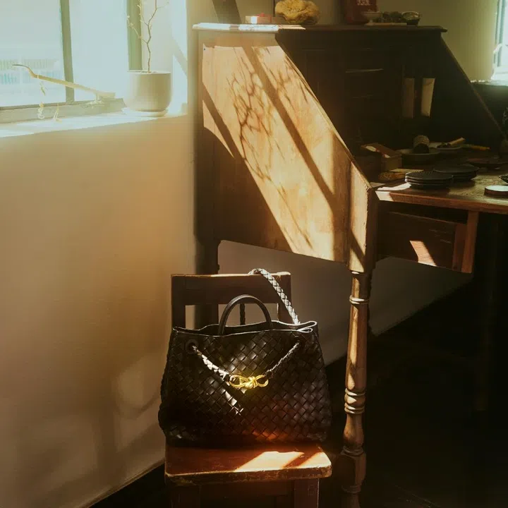 Bottega Veneta black Intrecciato Andiamo bag with gold knot detail on a wooden chair for F ZINE.