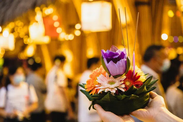 female hand holding krathong for Loi Krathong festival (krathong made with banana leaves, lotus flower, incenses and candle, floating on the water for good wishes)