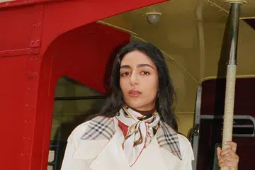 model wearing beige Burberry trench coat against red London bus