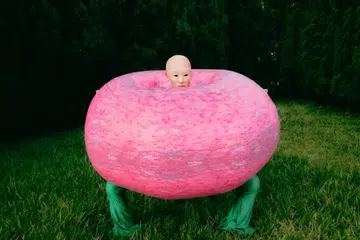 A surreal fashion photograph by Malaysian photographer Weeyang featuring a model in a large pink inflatable ring against a backdrop of pine trees.