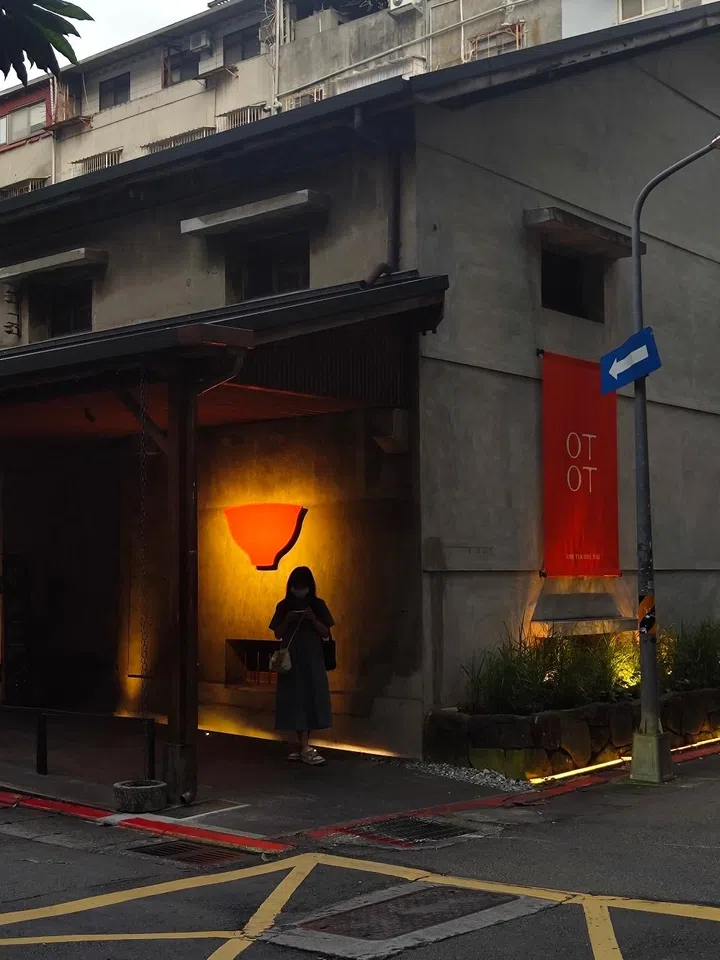 Minimalist tea house architecture at One Tea One Tile (OTOT) in Taipei, showcasing a modern industrial facade with warm accent lighting and clean design elements.