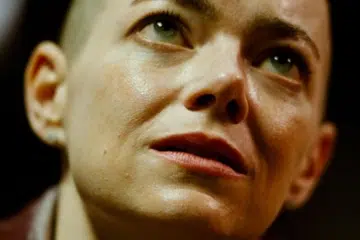 Emma Stone with a shaved head looking upward in a dramatic, close-up film still from Yorgos Lanthimos’s Bugonia.