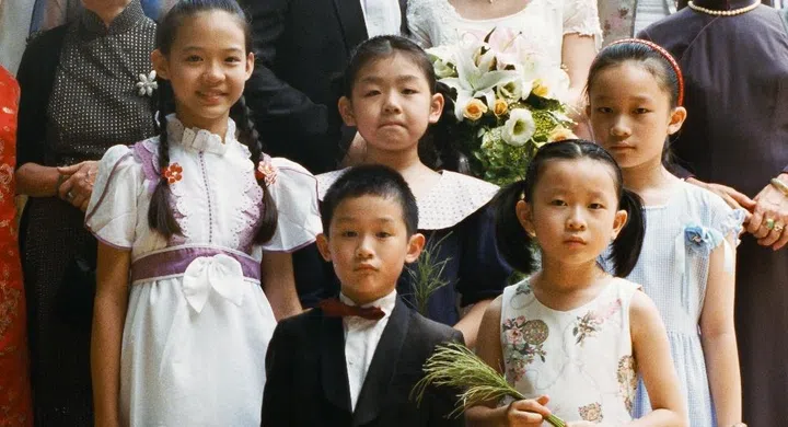 A film still from Edward Yang’s film Yi Yi, showing young Yang-Yang standing stoically in a tuxedo among children and wedding guests in a formal Taipei banquet hall.