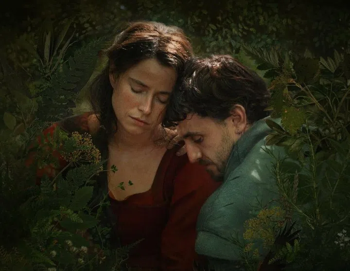 Jessie Buckley as Agnes and Paul Mescal as William in a promotional still from the film Hamnet. They are shown in a close embrace in a sun-dappled forest.