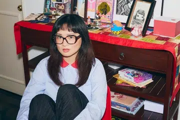 Viral TikTok anthropologist Ashley Chin, known for her deep dives into Singapore ghost stories, sits in an eclectic home setting.