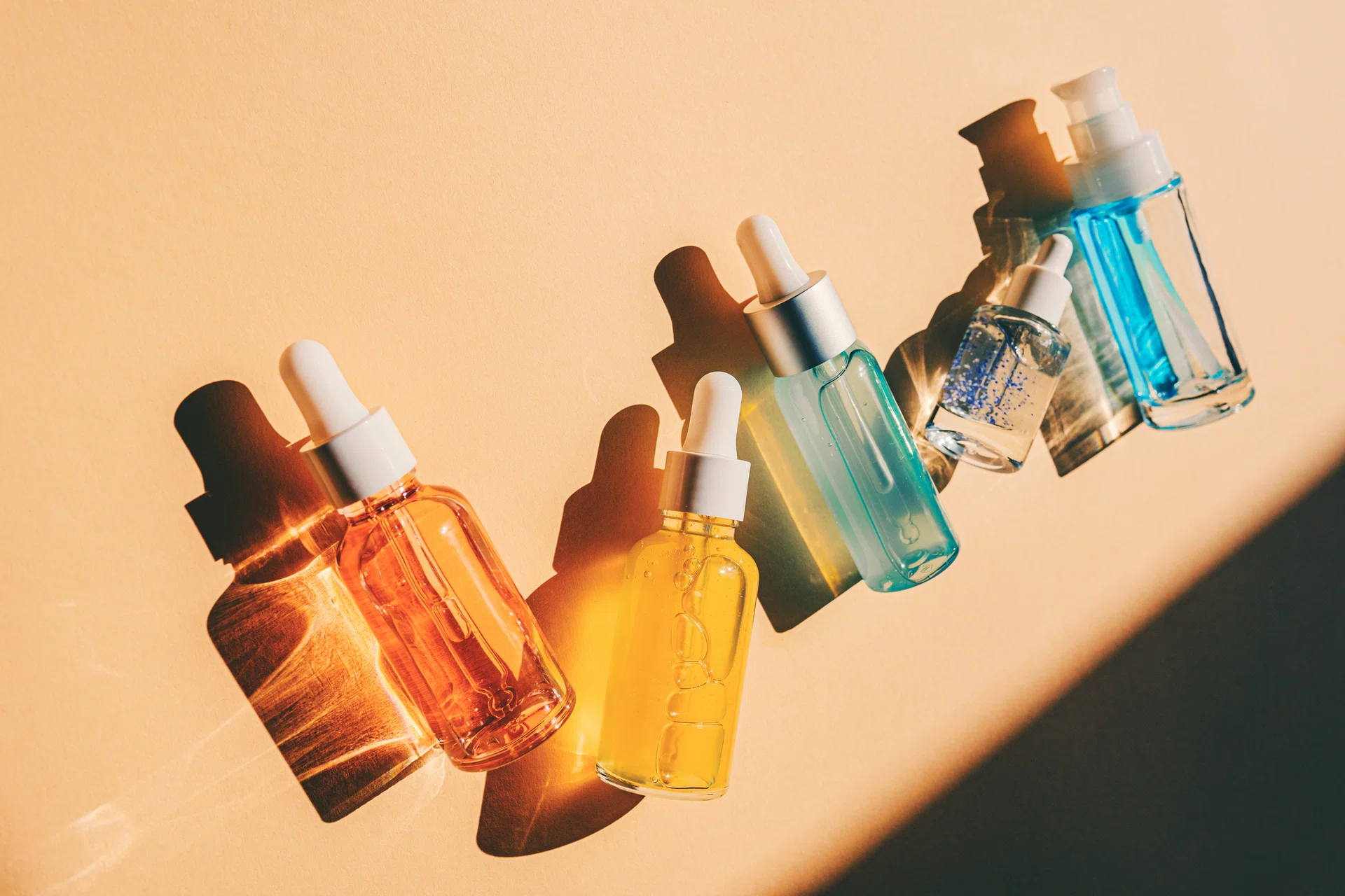 Assorted glass bottles with cosmetic liquids, serum or gel. Vibrant trendy background of cosmetic products, flat lay style