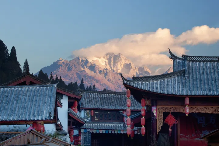 The Roofs of the old Town of Lijiang (UNESCO World Heritage) form a striking Contrast to the towering Jade Dragon Snow Mountain lit by the early Morning Sun
