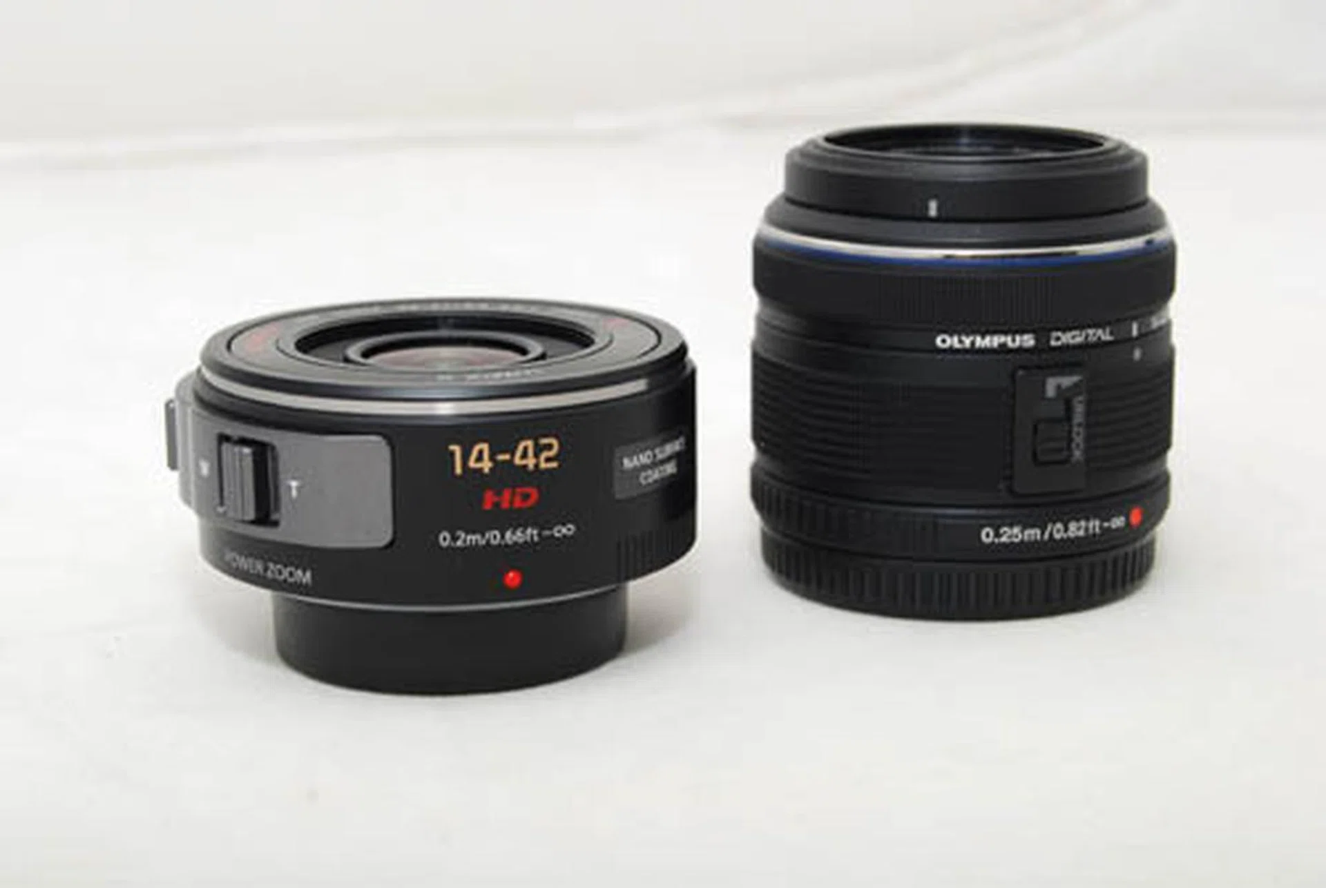 The X 14-42mm lens in comparison to a standard 14-42mm (an Olympus shown here). Both cameras have their lens protectors on below and the Olympus lens is locked.