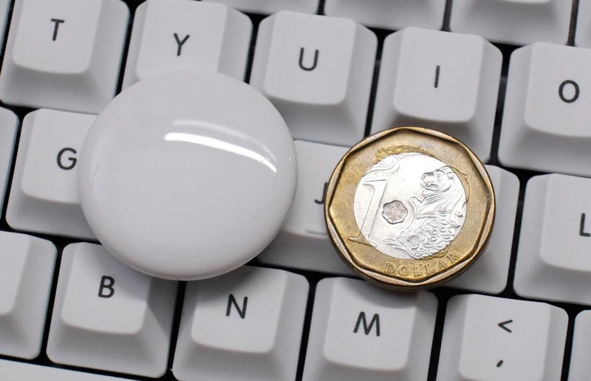 An AirTag next to a dollar coin.