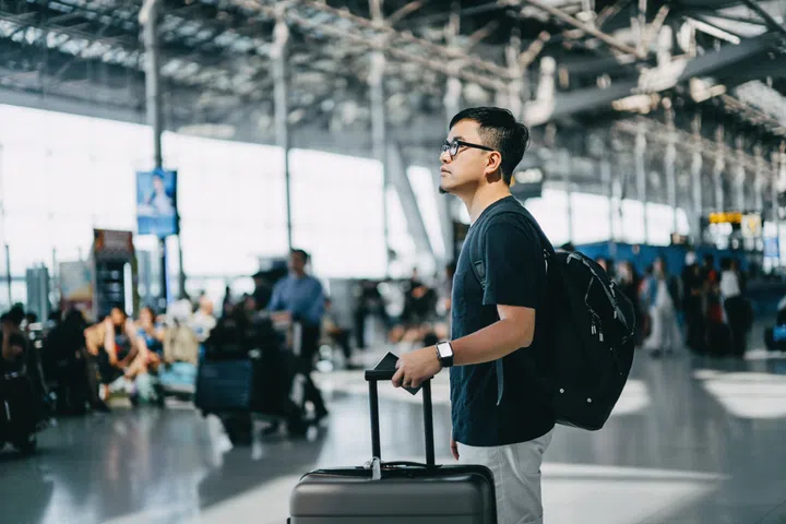 Young Asian male backpacker with passport and suitcase walking in the international airport hall