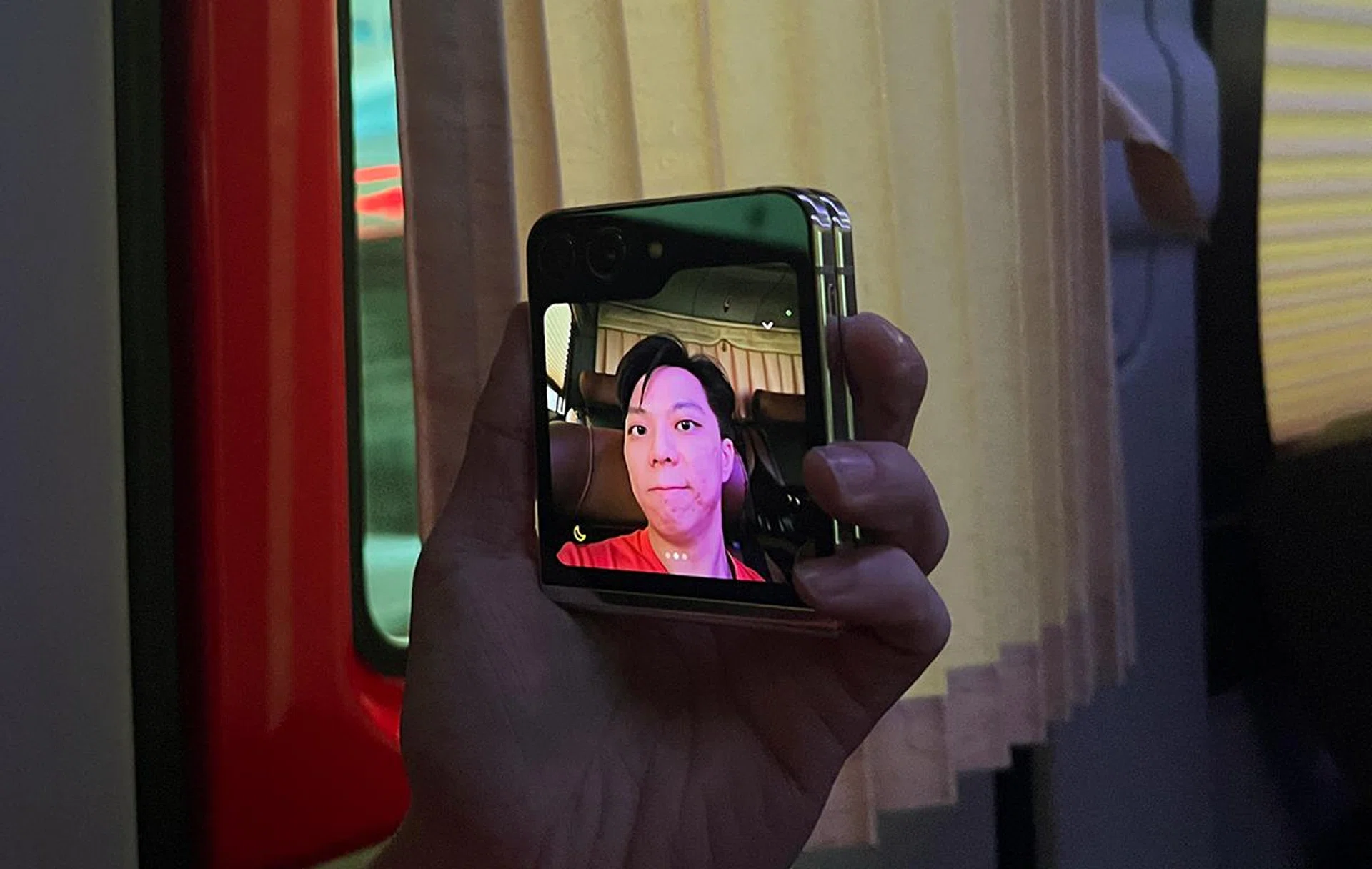 Samsung Galaxy Z Flip5 attempting a low-light selfie, inside a dimly-lit coach/bus. The side-mounted volume buttons act as its shutter.