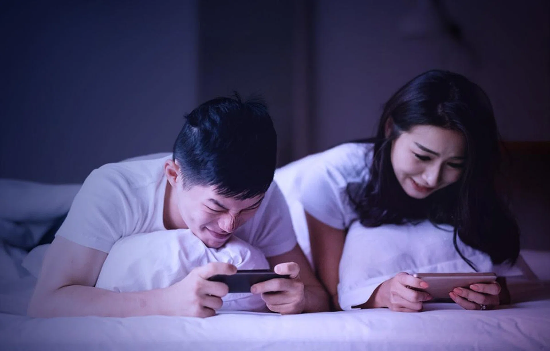 asian chinese couple lying on bed playing mobile game in the morning having fun
