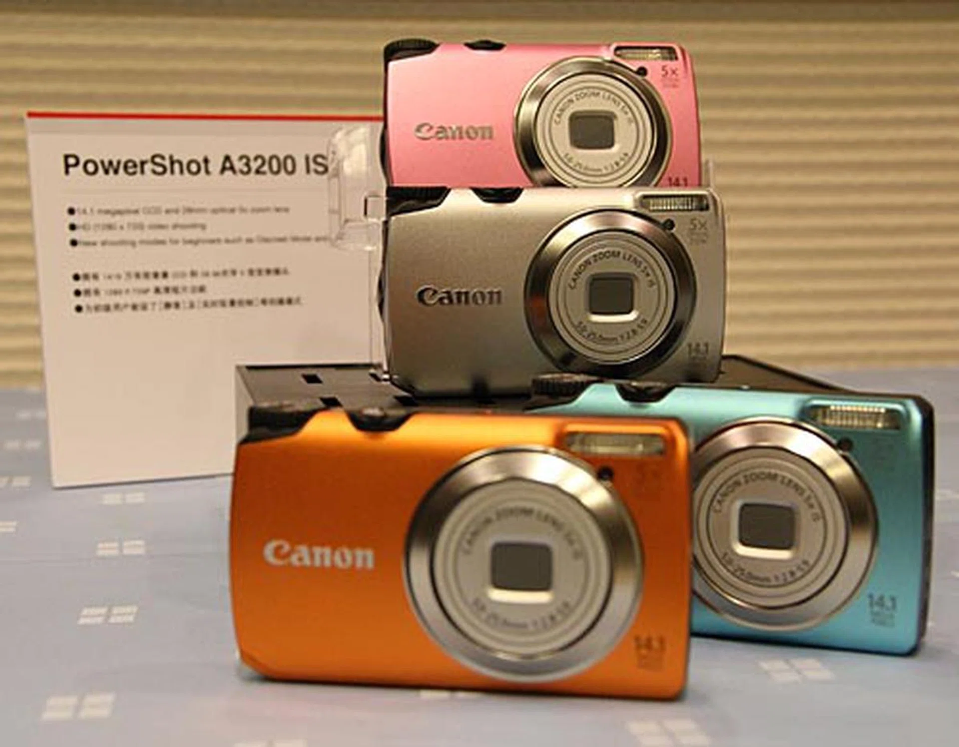 The 14.1-megapixel PowerShot A3200 IS comes with 28 mm lens with 5x optical zoom, 2.7-inch LCD, Smart Auto mode that detects 32 different scenes, Live Control (brightness, vividness, and color tone settings in one screen), six creative filters, Discreet mode (turns off flash and mute camera’s operational sounds), and 1280 x 720 HD movie recording. It’s available in pink, blue, orange, and silver.