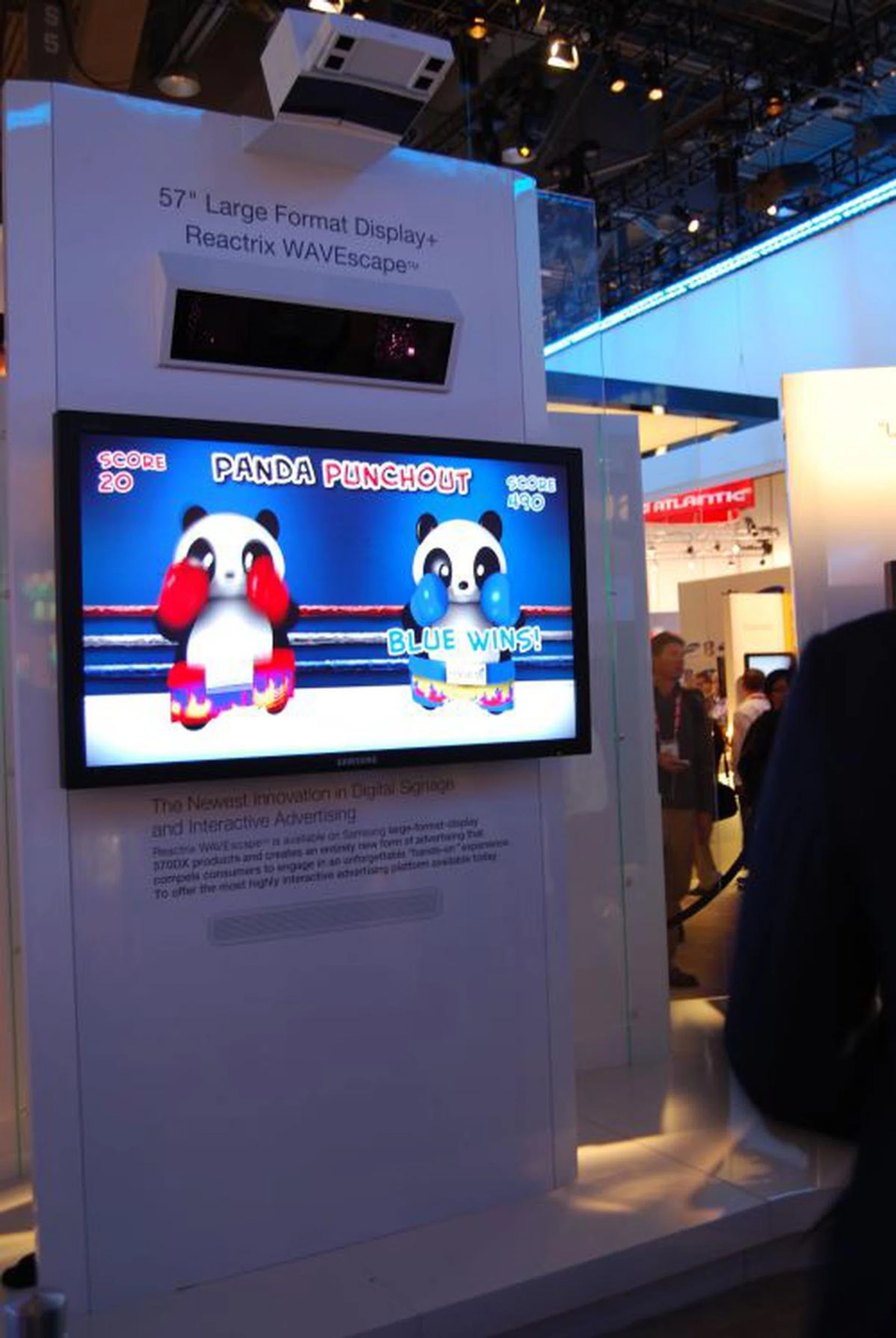 Samsung teamed up with Reactrix to demonstrate what could be a marketer's dream. Applicable as a form of interactive digital signage at retail outlets, shopping malls and so on, the Reactrix WAVEscape system is paired up with a 57" large format Samsung display. Passers-by can wave their hands and interact with various objects on the screen based on an overhead mounted sensor that detects hand movements within a certain zone about a few inches in front of the screen.  