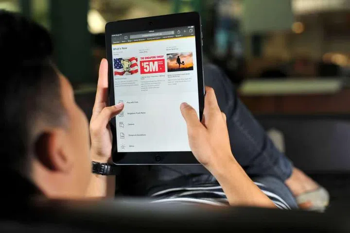 Posed photograph of a man looking at the Singapore Pools website on a tablet. Credit: ST FILE