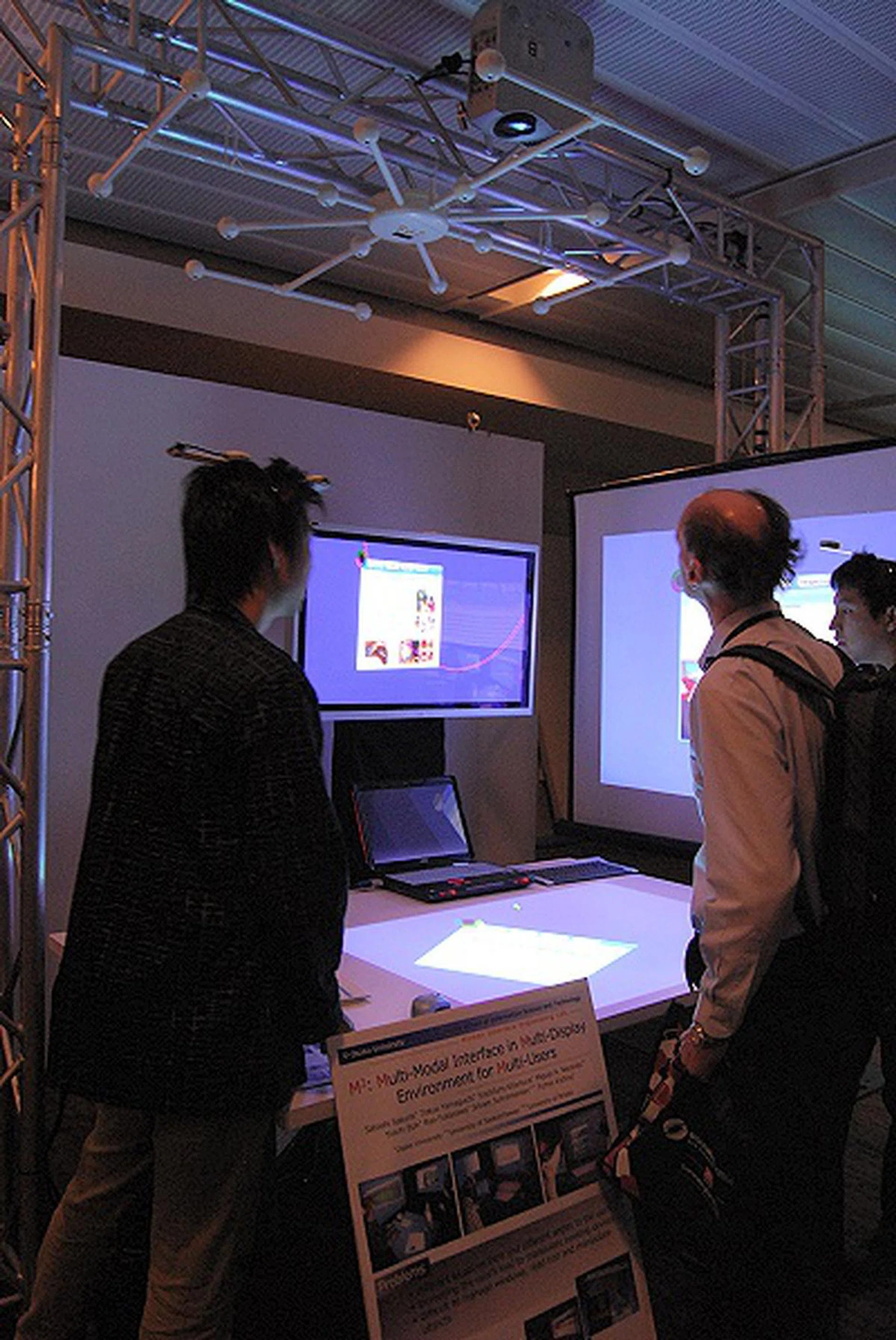 A prototype model built and engineered by the graduate students of Osaka University and others in Japan as a joint collaboration, this is a demonstration of a multi-model interface in multi-display environment for multi-users (also fondly called as M3 by the students). With a simple head mounted unit by each user, the system actually has a sensor array on top of the work area that detects the body movements and hand gestures of each user to display a perspective-aware window that each user is manipulating across multiple screens.