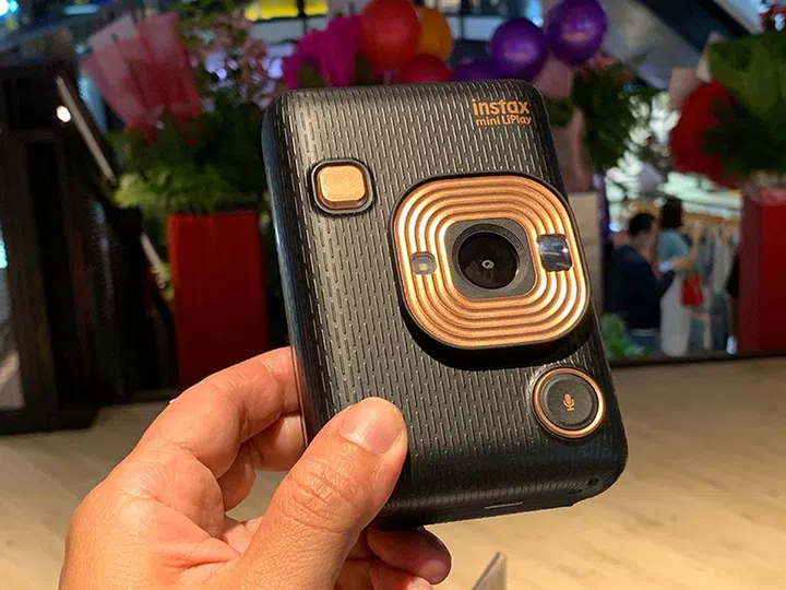 The shutter release button is located at the front of the camera. At the opposite end is the button for triggering the audio-recording function.