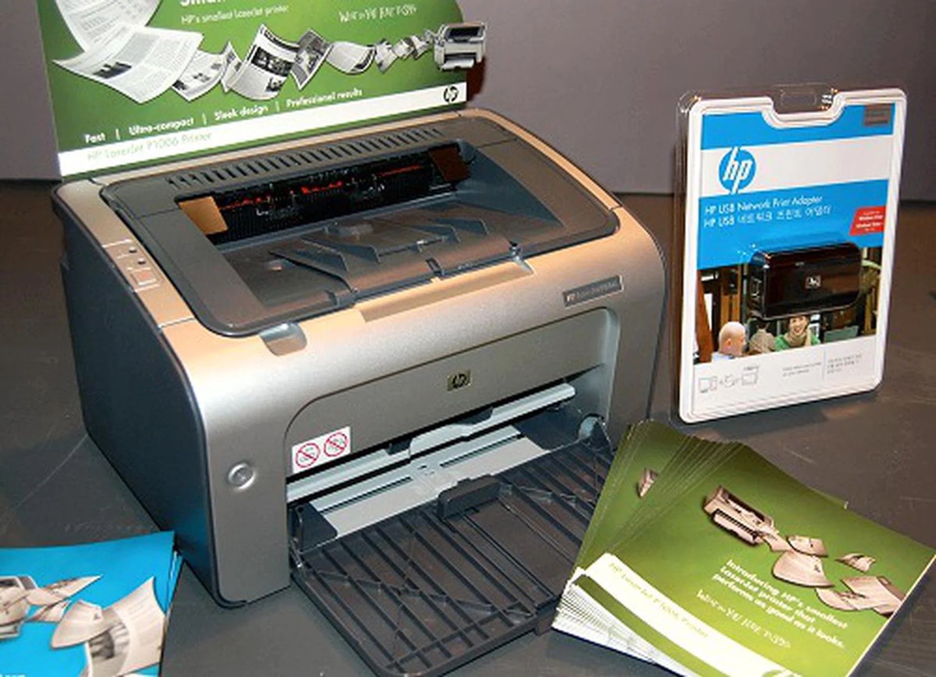  This LaserJet P1006 is chic petite looking personal business laser printer that's not only friendly on the wallet, but also user-friendly and fast. Using the new CPT mono toner technology, it can also deliver quality prints at 16 pages per minute with the first page out in less than 8.5 seconds. There's also the P1005 variant for the more budget conscious user which ditches the nice color motif for the dull PC beige color and foregoes any user controls on the printer face. The blue package next to the printer is HP's relatively new USB network printer adapter.  